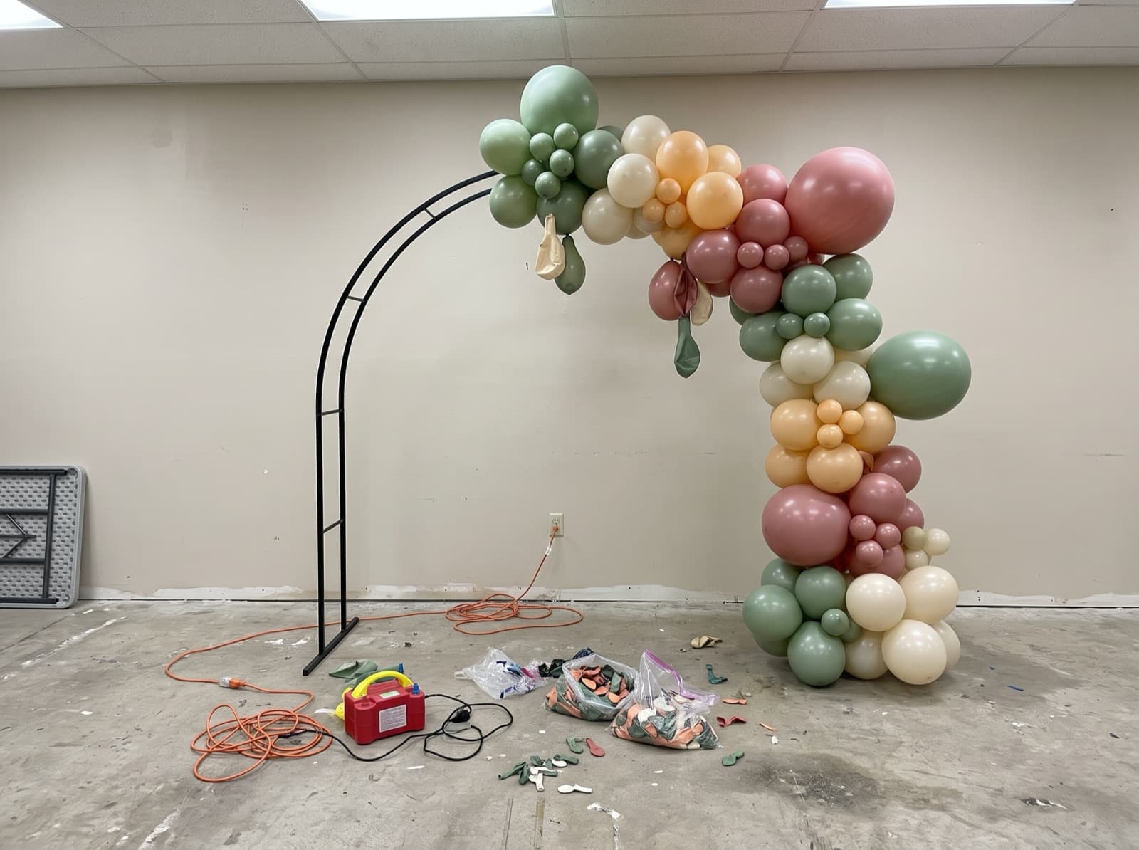 Half-finished organic garland on a metal arch frame during setup in an empty event room
