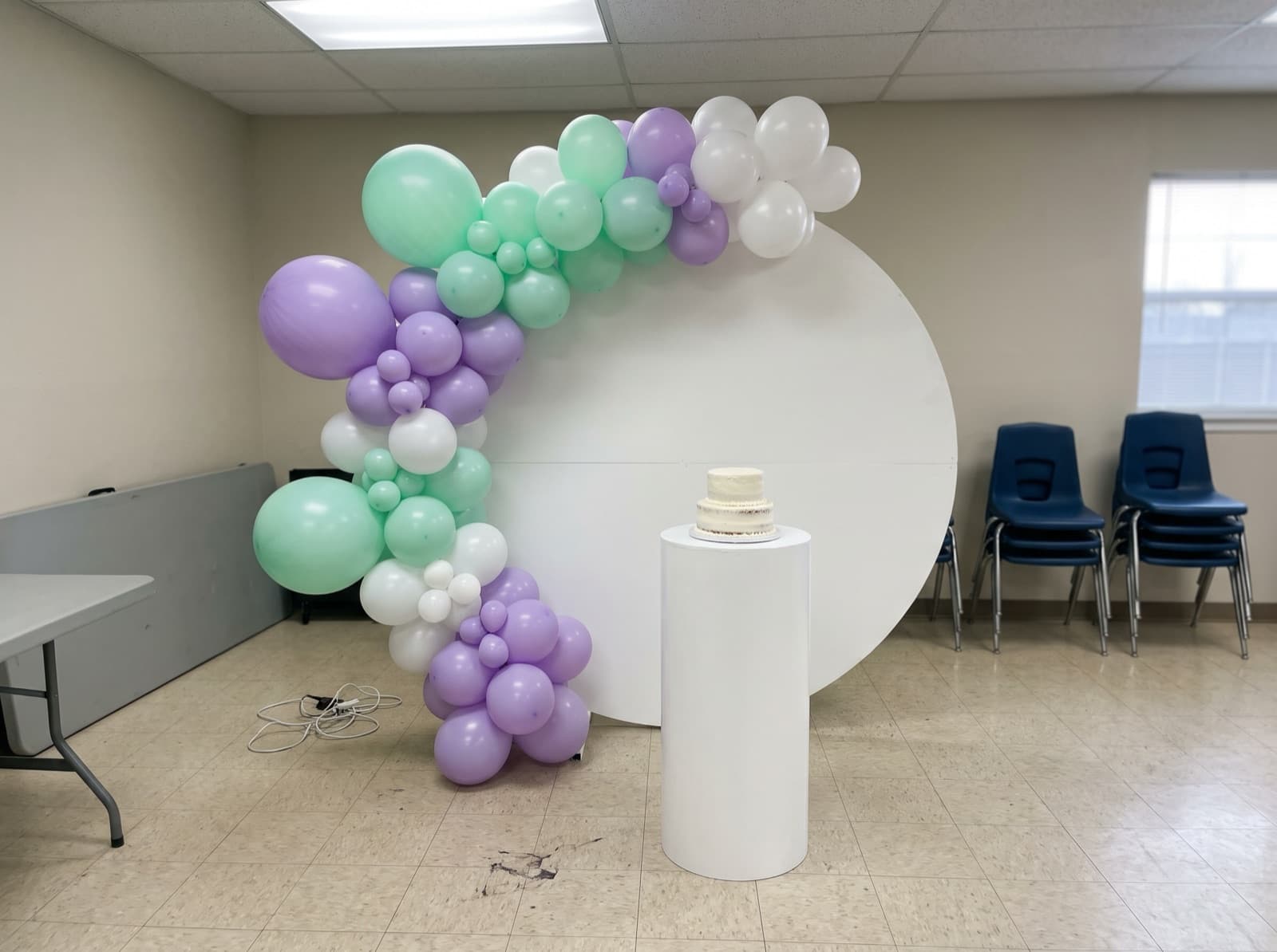 Round balloon backdrop with a lavender and mint organic garland and a cake pedestal at a Dallas birthday party