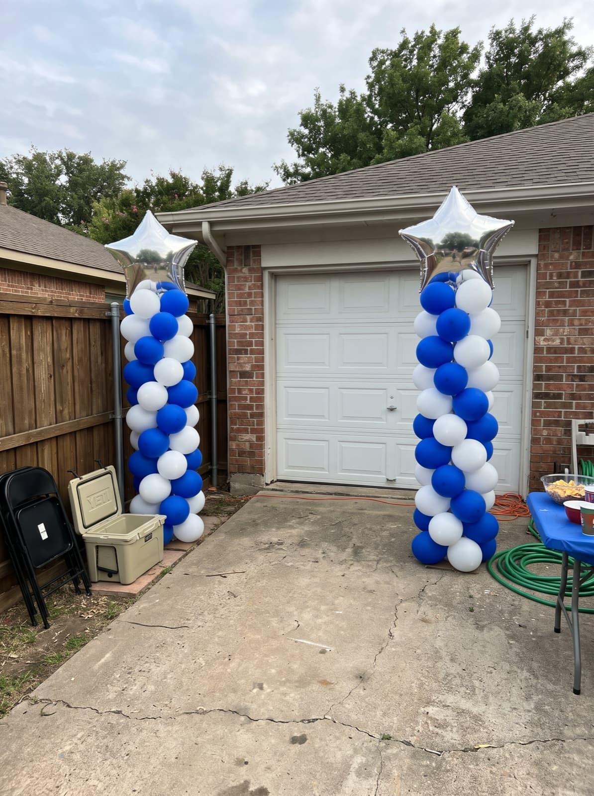 Blue and white spiral balloon columns topped with silver stars beside a garage door at a Dallas grad party