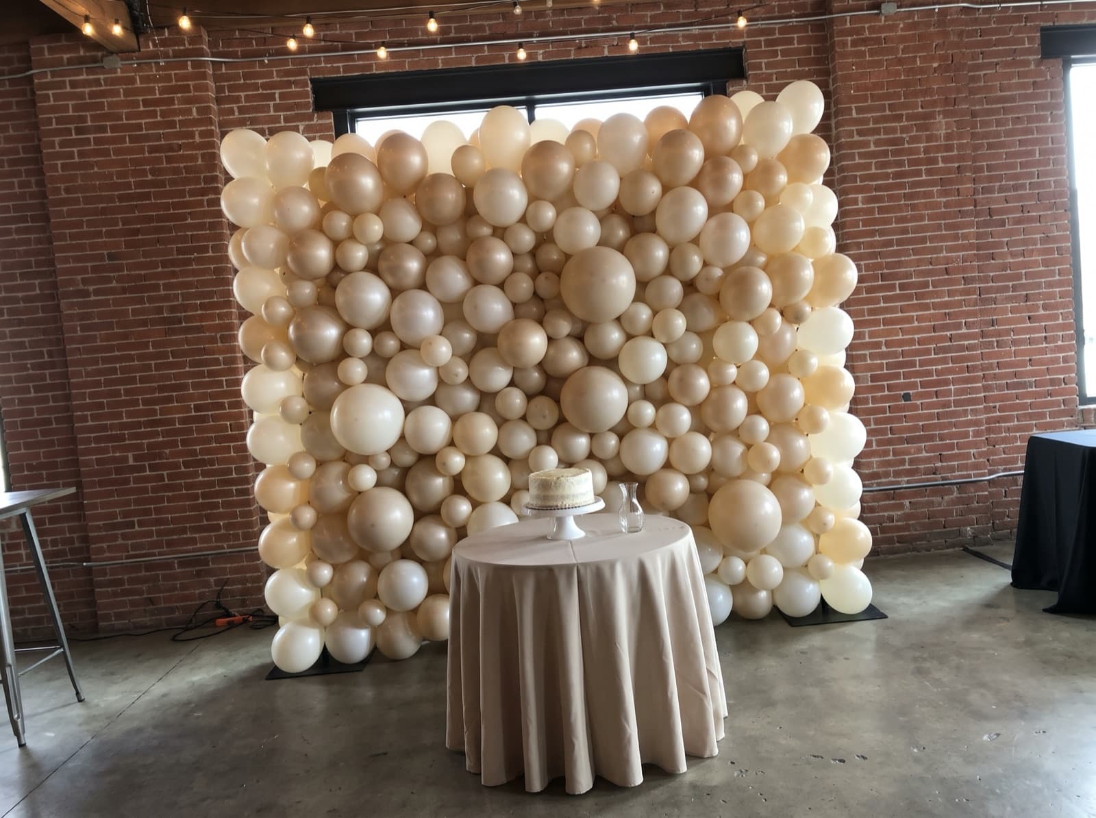 Organic balloon wall in ivory, pearl and champagne behind a cake table in a Dallas event space
