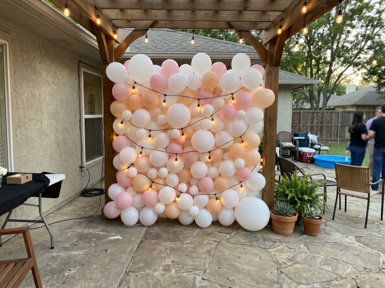White and blush balloon wall laced with string lights on a patio at night